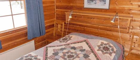 A cozy room with a wooden interior, a bed with a floral quilt, a window with a view, and a painting on the wall.