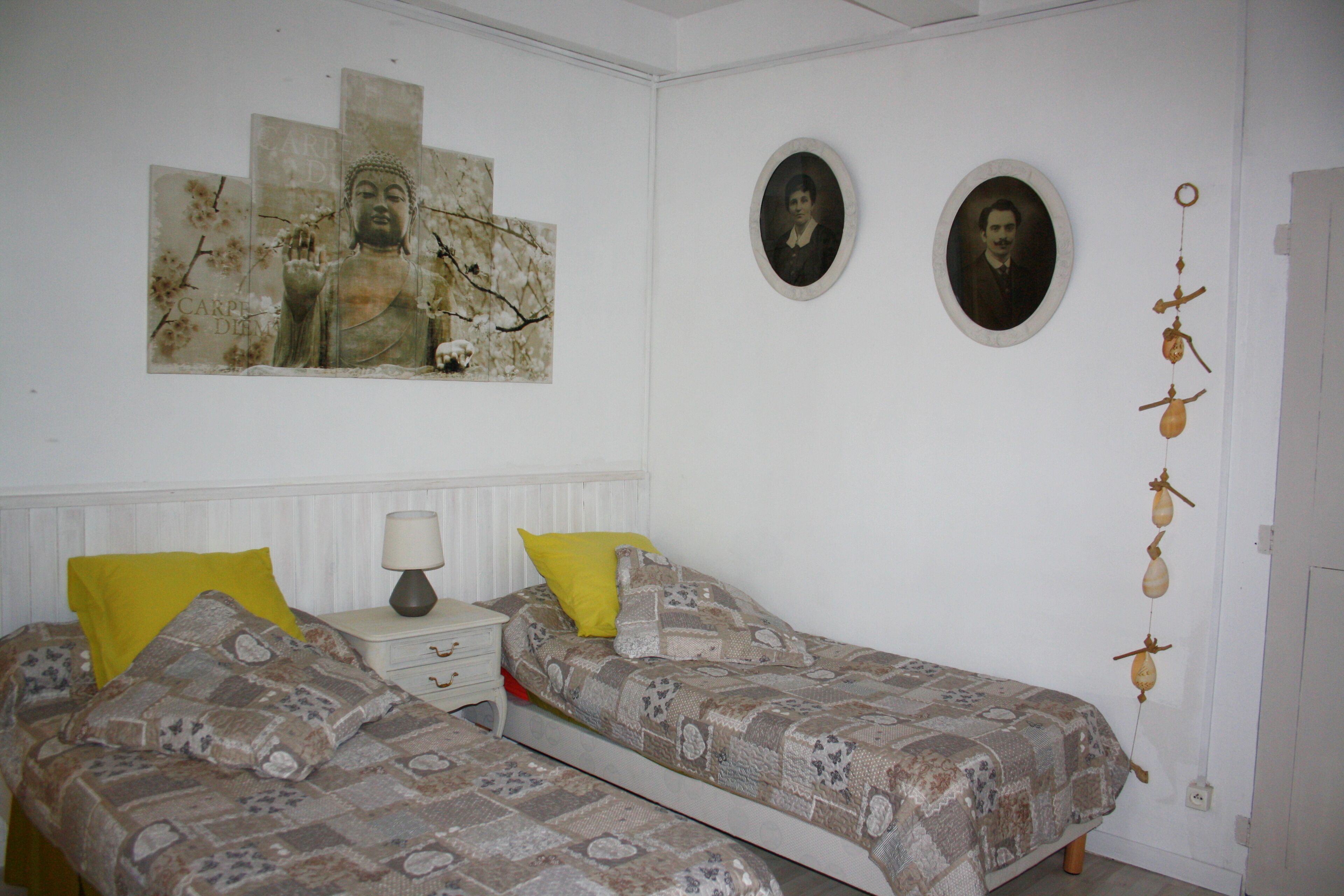 A bedroom with two beds, a nightstand, a lamp, and wall decorations including framed pictures and a hanging ornament.