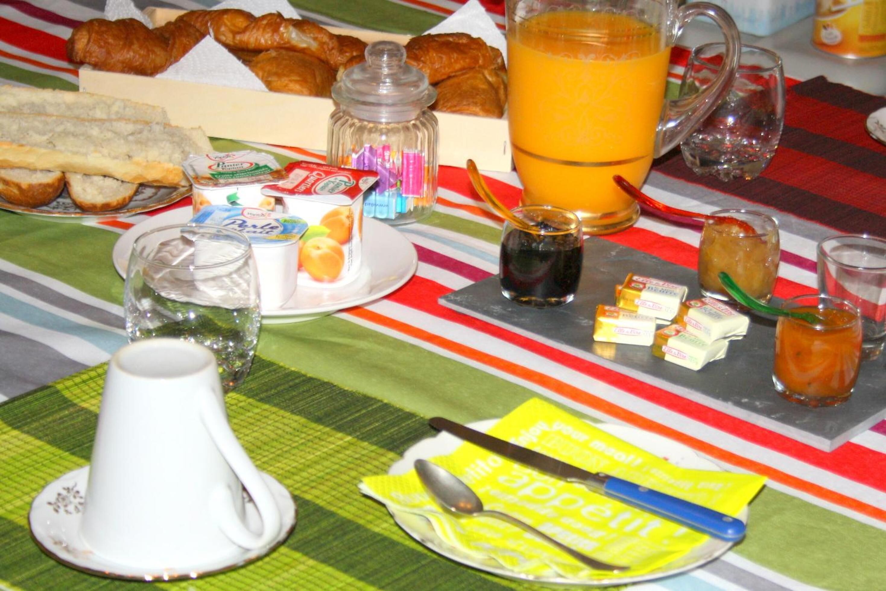 Una mesa de desayuno con cruasanes, jugo y diferentes condimentos.