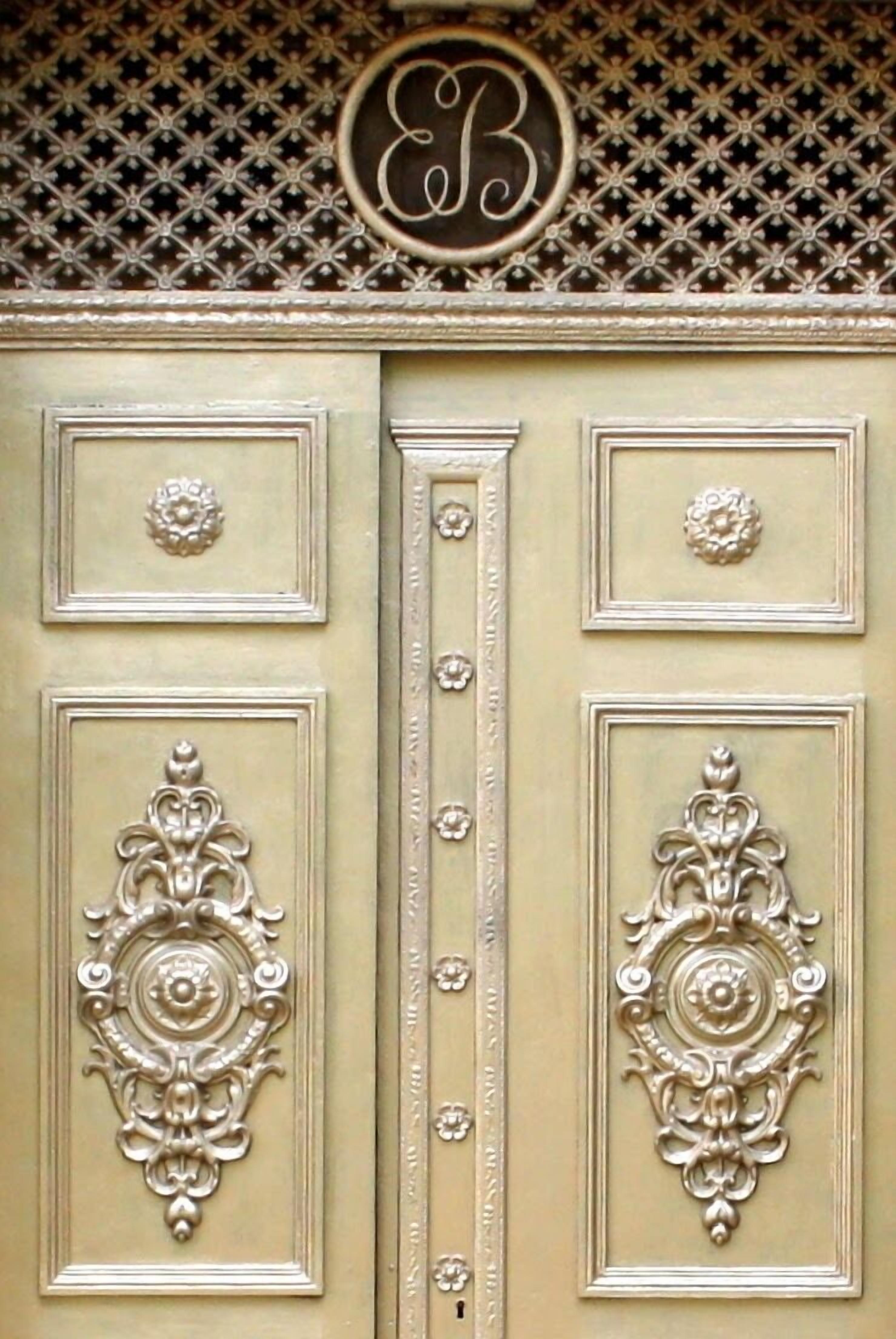 A double door with ornate metal handles and a letter 'B' above it.