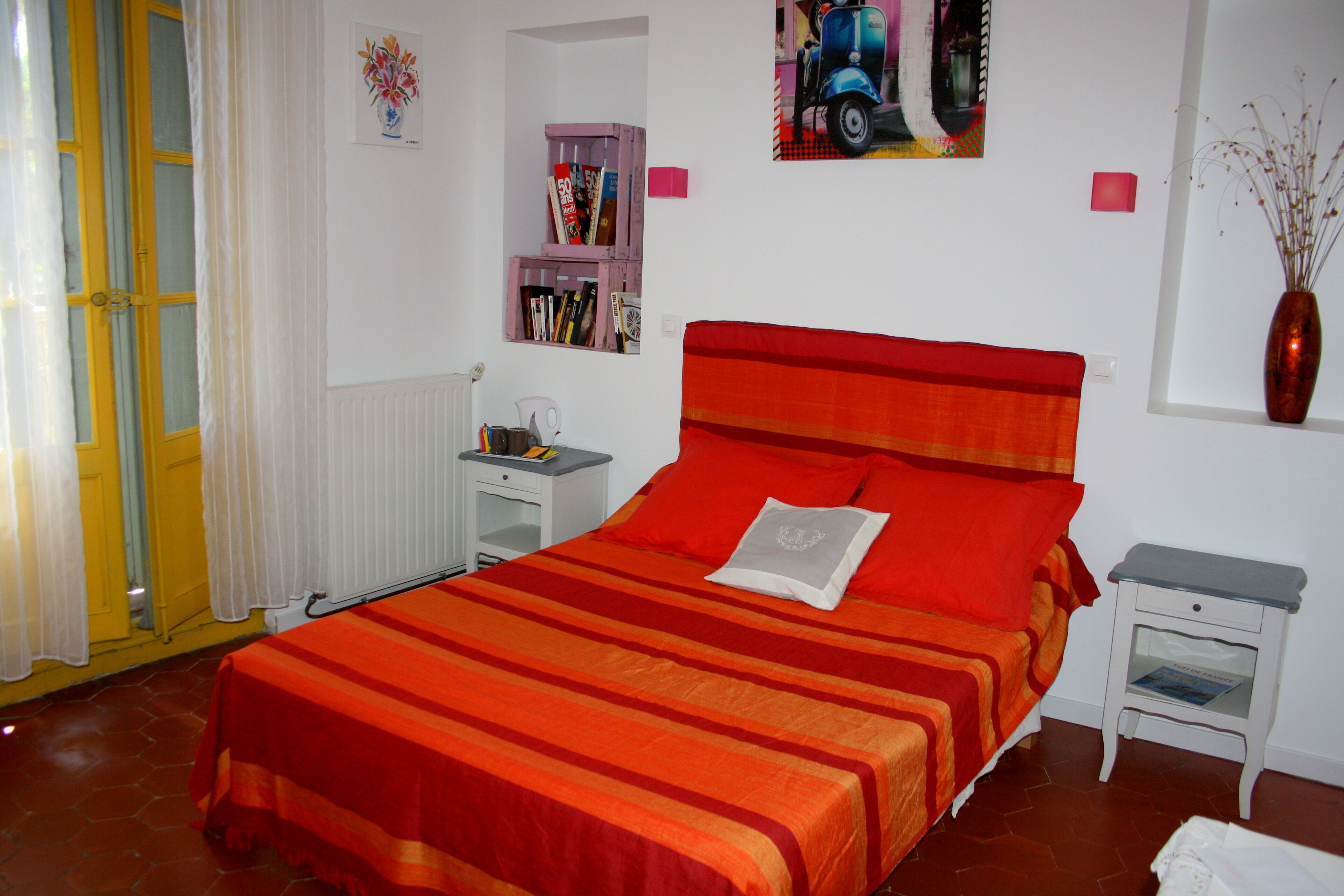 Un dormitorio con cama, mesita de noche, estantería y ventana con un florero.