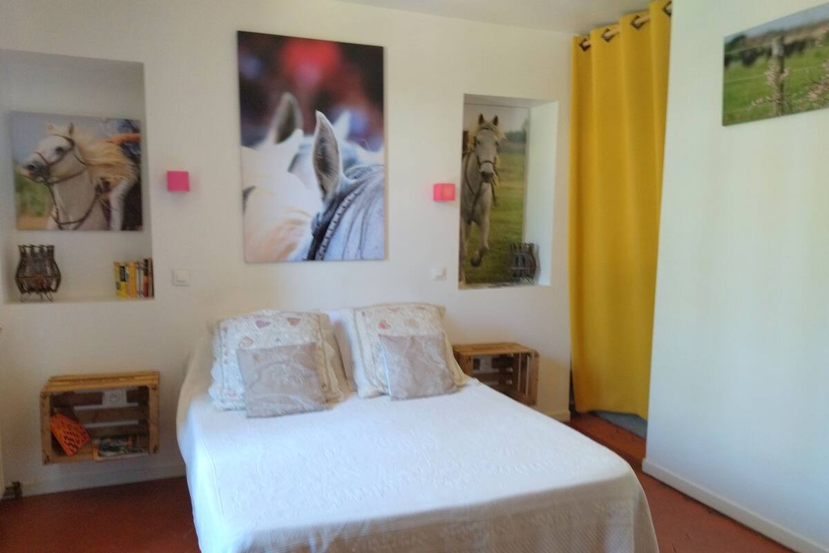 Ein Schlafzimmer mit einem Bett, zwei an der Wand befestigten Gemälden von Pferden, einem Holznachttisch und einem gelben Vorhang.
