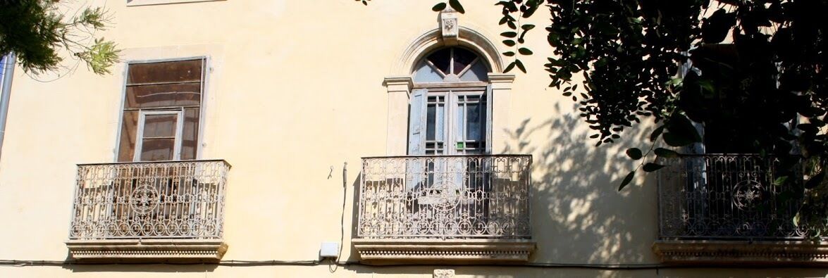 Fachada de edificio con dos balcones, cada uno con barandillas de metal ornamentadas y un ventanal pequeño en la parte superior.