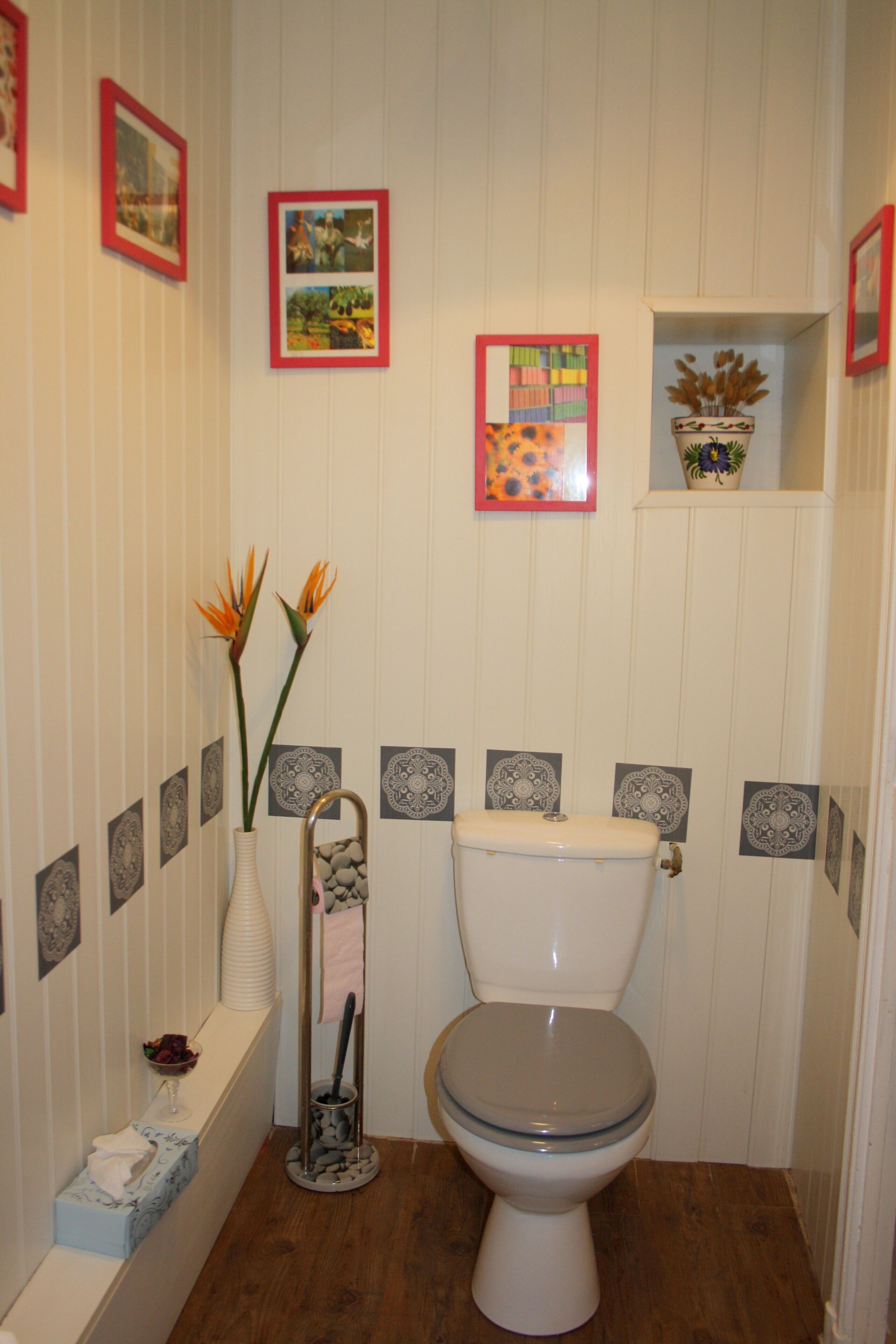 Een badkamer met een toilet, een vaas met bloemen en decoratieve tegels aan de muren.