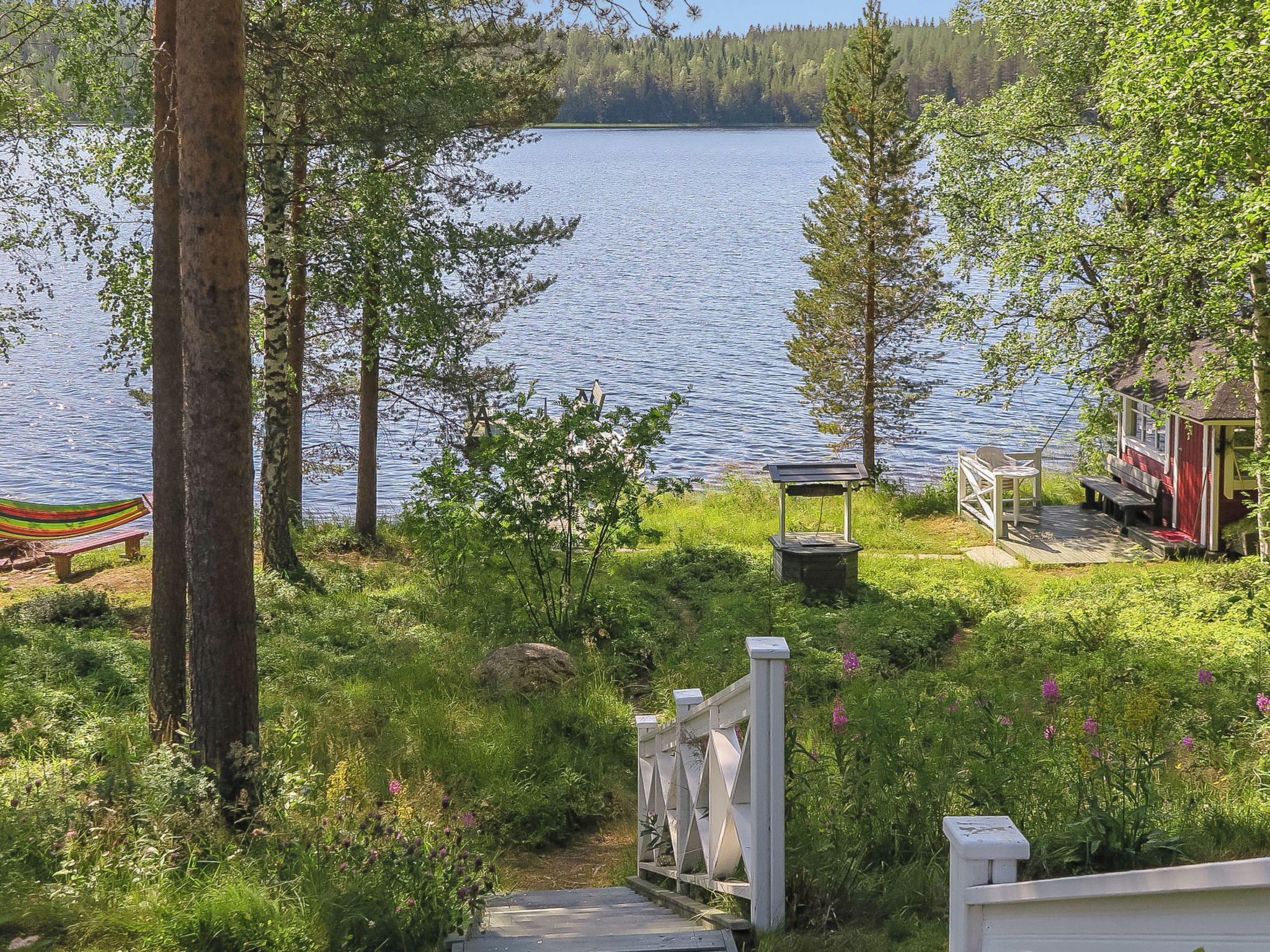 A lakeside property with a wooden deck, a gazebo, and a small cabin.