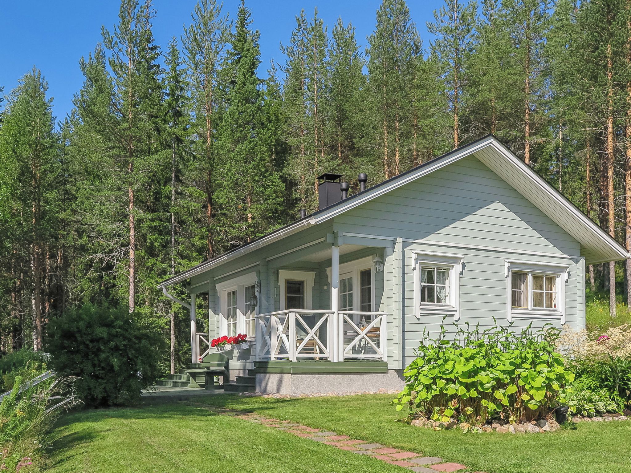 Een lichtblauwe woning met een veranda, omringd door een bos.