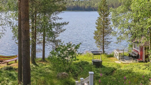 Una cabaña junto al lago con un porche, un banco y un cobertizo pequeño.