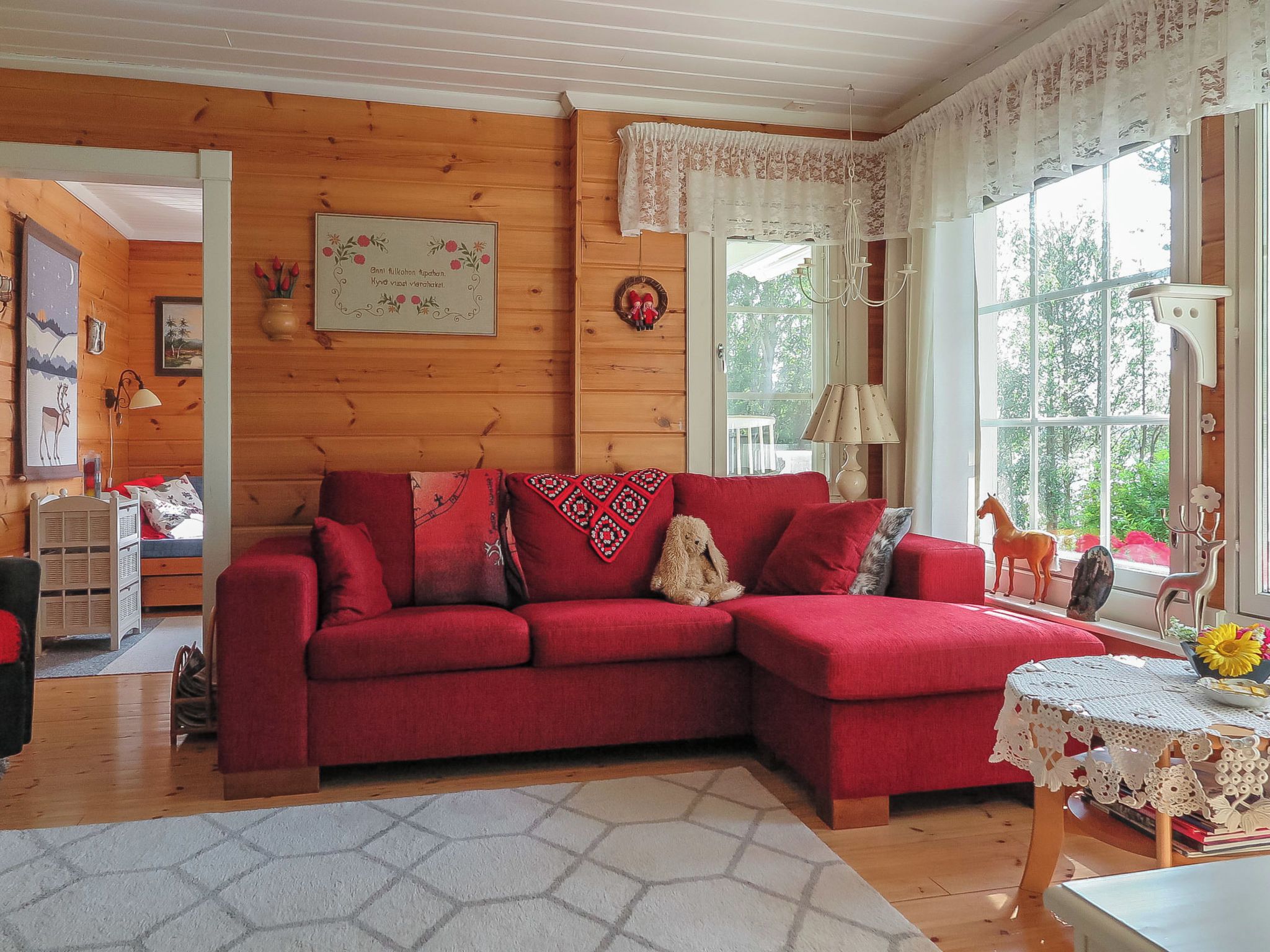 A cozy living room with a red sofa, a small table with a lace tablecloth, and a window with curtains.