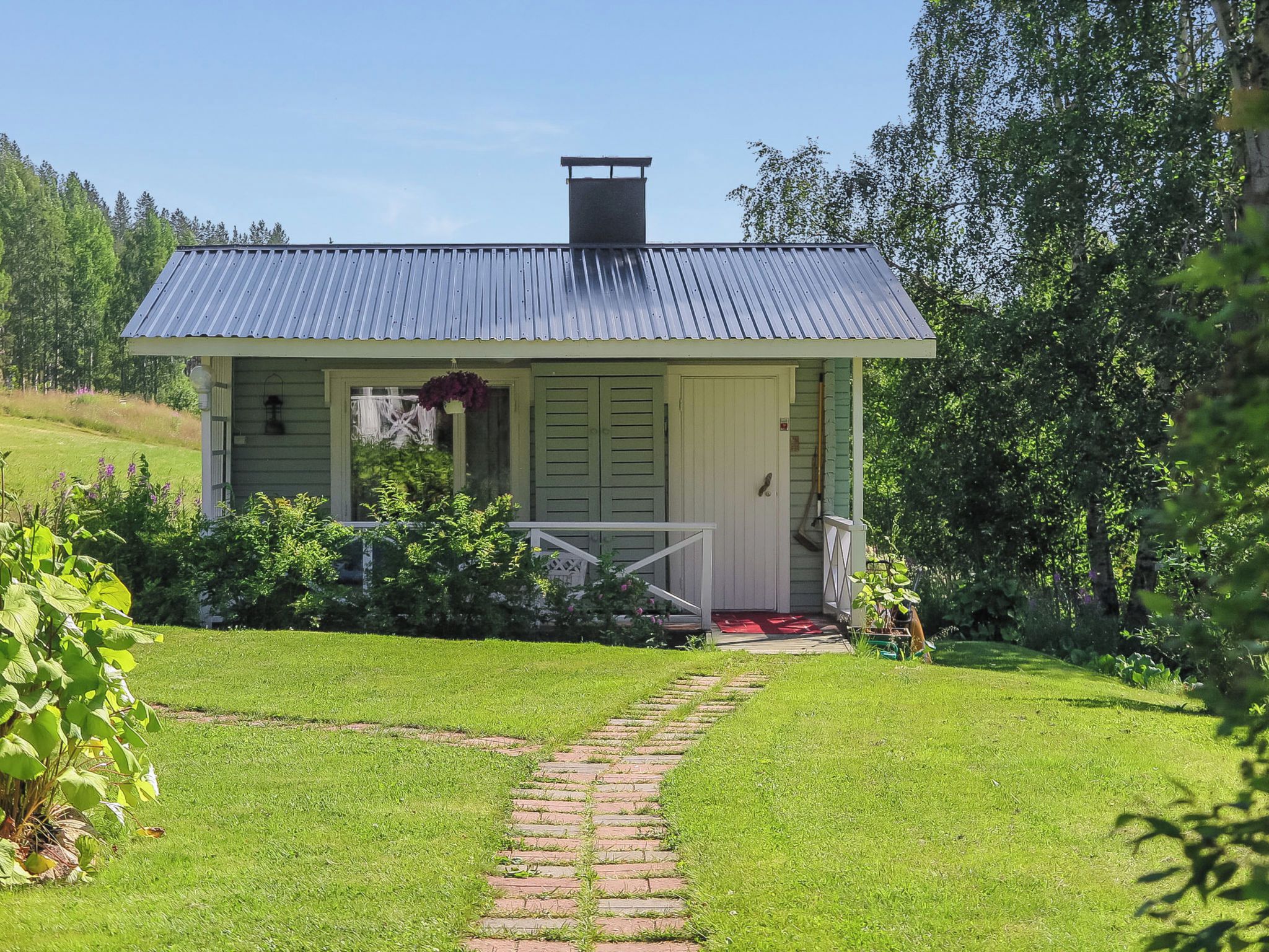 A small, single-story house with a metal roof, a front porch, and a brick pathway leading to the entrance.