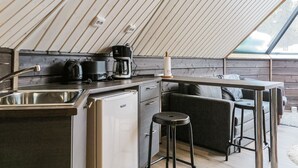 Une cuisine compacte équipée d’un réfrigérateur, d’une machine à café et de tabourets de bar.