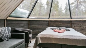 Une chambre confortable dans un chalet, dotée d’une grande lucarne, d’un lit avec des oreillers et d’un coin salon avec un canapé et des fauteuils.