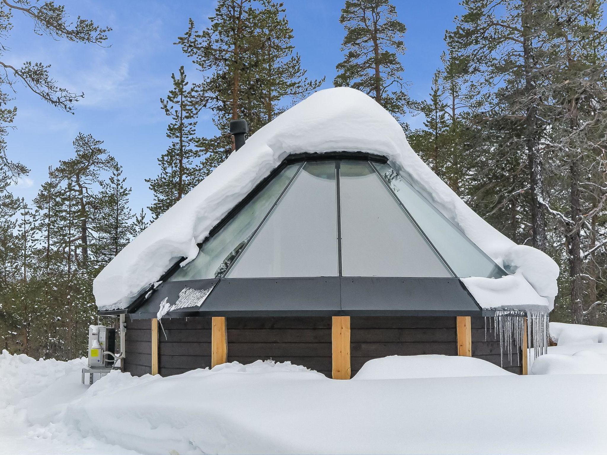 A snow-covered cabin with a large window, surrounded by trees.
