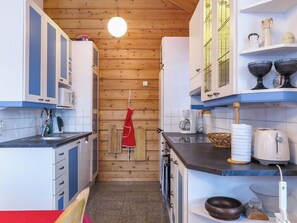 Une cuisine de taille réduite avec des murs en bois, des armoires blanches et un tablier rouge accroché au mur.