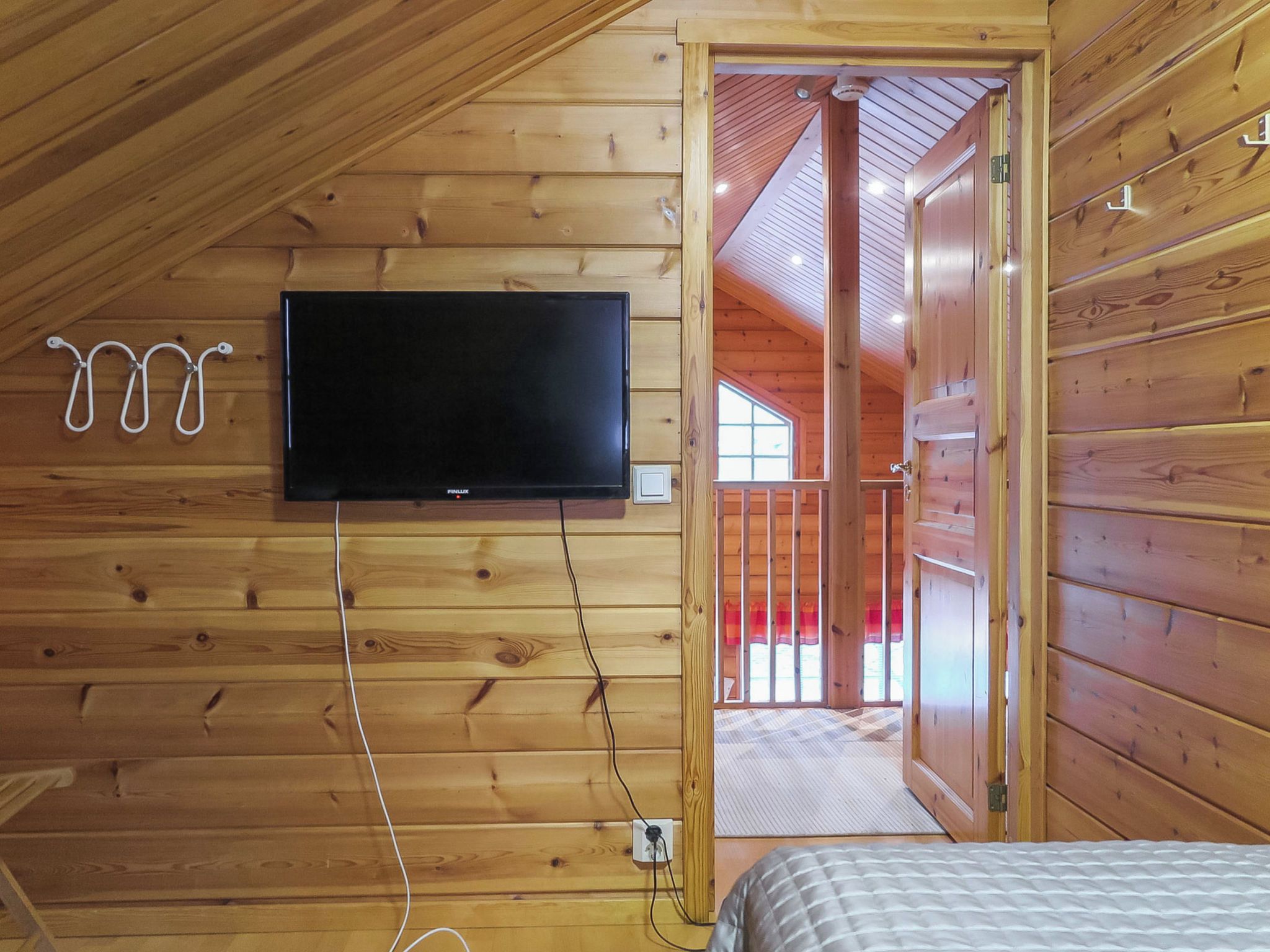 Una cabana de fusta amb televisió penjada, un llit i una porta que dona a zona exterior.