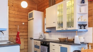 A kitchen with wooden walls, white cabinets, a refrigerator, a coffee maker, and a red table.