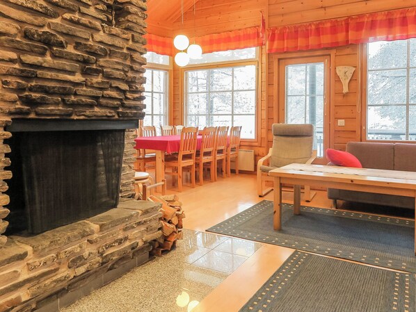 A cozy interior with a stone fireplace, a dining area with a red tablecloth, and a sofa with a cushion. - Riekkoluosto by Interhome (Sodankylä)