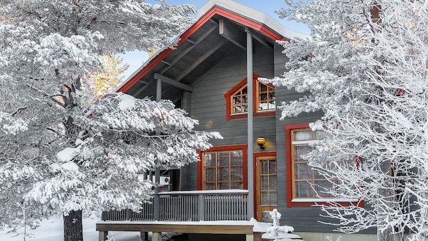 A two-story house with a red and gray exterior, a covered porch, and snow-covered trees.