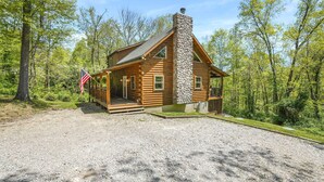 A log cabin with a stone chimney, surrounded by trees and a gravel driveway. - Bobcat Bluff-Hocking Hills State Park-Covered Hot Tub-Firepit-Pool Table-WiFi  (Logan)