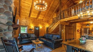 A log cabin interior with a wooden staircase, leather sofas, a dining table, and a stone wall. - Bobcat Bluff-Hocking Hills State Park-Covered Hot Tub-Firepit-Pool Table-WiFi  (Logan)