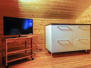 A wooden-paneled room with a television on a wooden stand and a white cabinet with drawers.
