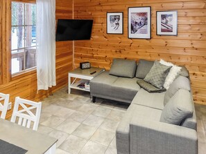 A cozy living room with a grey sofa, a flat-screen TV mounted on the wall, and a wooden floor.