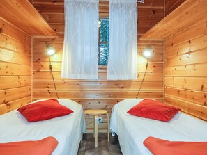 Una habitación tipo cabaña con dos camas, un taburete pequeño y una ventana con cortinas.