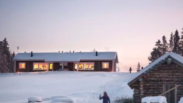 Une cabane en rondins dont le toit est recouvert de neige, et une personne qui marche dans la neige.