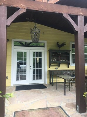A covered patio with a stone floor, a white door, and a wooden bench. - " Casa Grande" Hot Tub_ Indoor Basketball + Movie (Brevard)