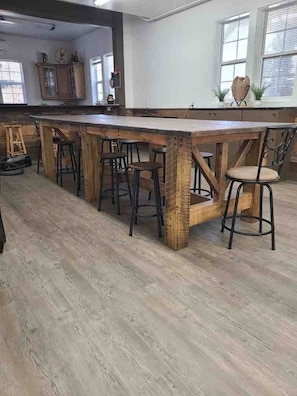 A kitchen with a long wooden island, stools, and a view of the adjacent dining area.