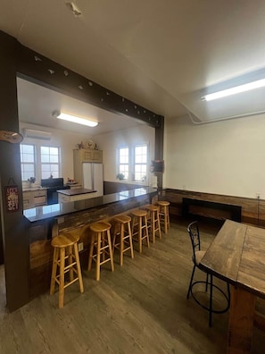 A modern kitchen with a bar area, wooden stools, and a dining table.
