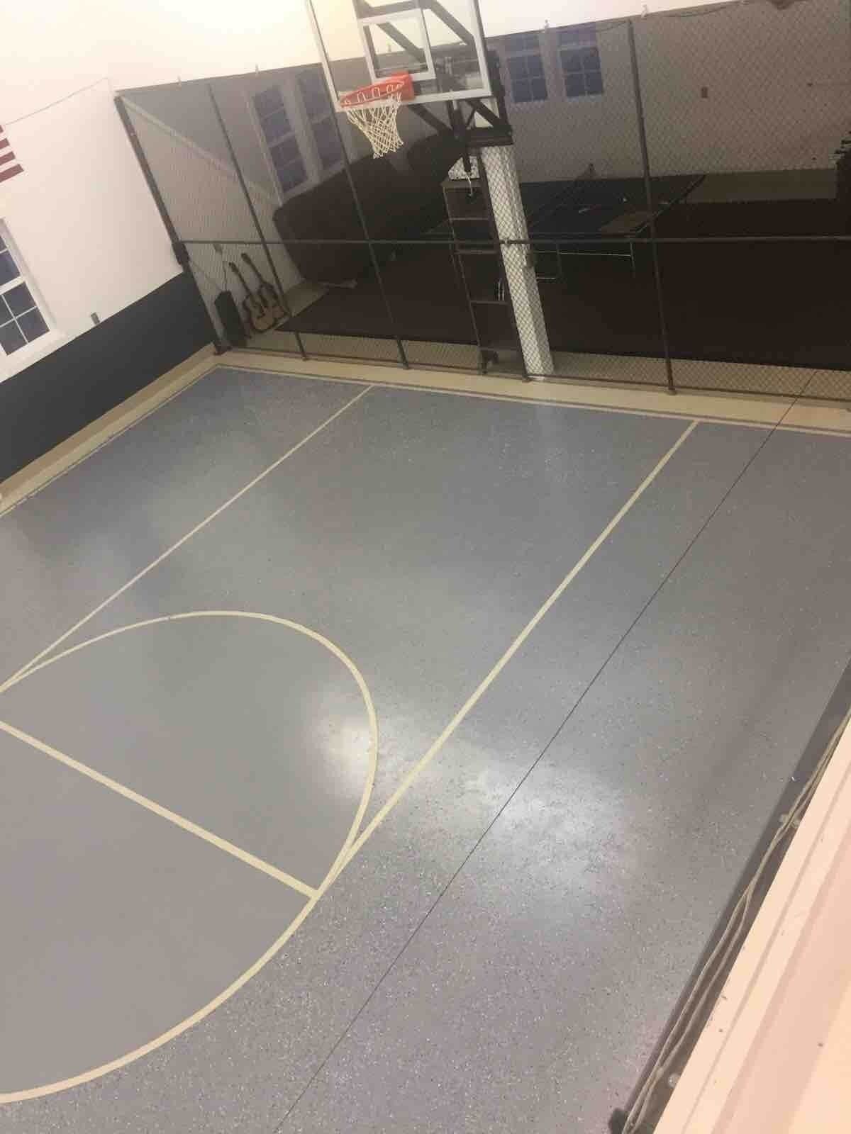 Eine Sporthalle mit einem Basketballkorb, Netz und einer Wand mit Fenstern.