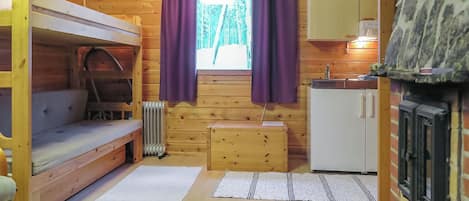 Ein gemütliches Blockhaus mit Etagenbett, einer kleinen Küchenzeile und einem Kamin.