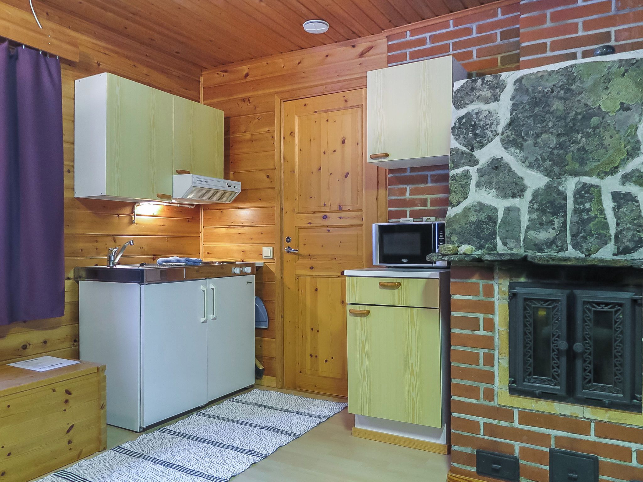 Eine kleine Küche mit Holzschränken, einer Mikrowelle und einem Kamin aus Naturstein.