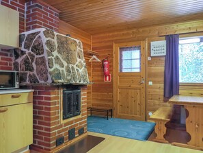 A cozy cabin interior with a stone fireplace, wooden walls, a small kitchen area, and a wooden dining table. - Lemmenliekki 3 by Interhome (Inari)