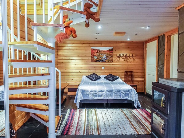 A bedroom with a bed, a wooden staircase, a fireplace, and a wall-mounted shelf.