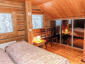 A cozy wooden cabin room with a bed, a table with a lamp, and a sliding glass door leading to a balcony. - Ylikyrön mökki by Interhome (Enontekiö)