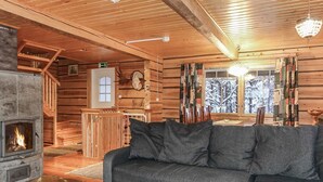 Interior acogedor de una cabaña con chimenea de piedra, paredes de madera, un sofá y una ventana con vistas nevadas.