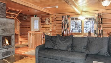 A log cabin interior with a fireplace, wooden walls, a sofa, and a dining area.