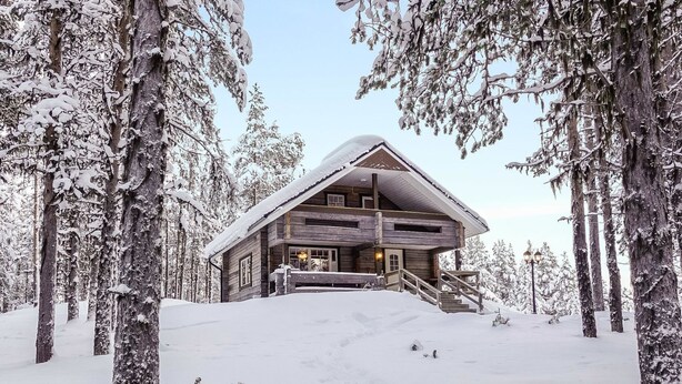 Una cabaña de troncos con un techo pronunciado, rodeada de árboles cubiertos de nieve.