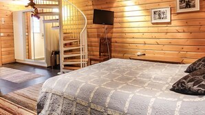 Una habitación acogedora con una escalera espiral, una cama con colcha estampada, paredes de madera y un televisor montado.