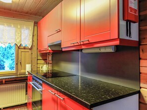 A kitchen with red cabinets, a black countertop, and a window with a view of trees.