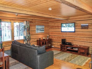 A log cabin interior with a sofa, television, and wooden walls.
