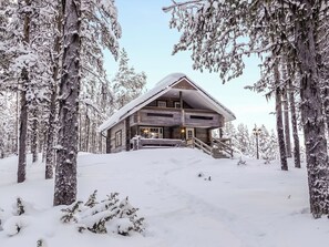 A wooden cabin with a sloped roof, surrounded by snow-covered trees.