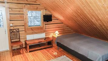Un acogedor dormitorio en el ático con techo inclinado, paredes de madera, una cama, un televisor, una silla y una pequeña mesa.