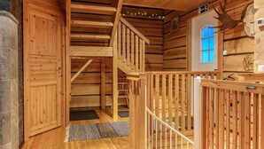 Un interior de madera con una escalera que conduce a un nivel superior, una puerta con ventanal y decoraciones de cornamenta en la pared.
