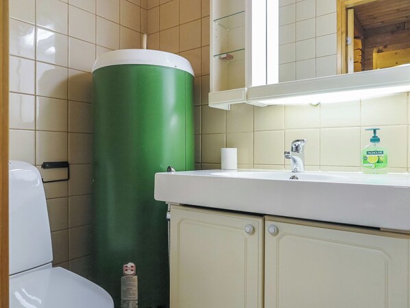 A bathroom with a toilet, a green cylindrical object, a sink with a faucet, and a mirror above the mirror.