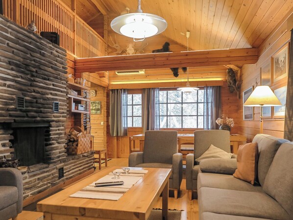 L’intérieur d’un chalet chaleureux, avec une cheminée en pierre, des meubles en bois et une grande fenêtre.
