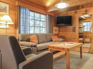 A cozy cabin interior with a sofa, a table, a television, and a window with curtains.