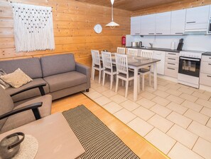 Una cocina moderna con gabinetes blancos y un horno empotrado, un comedor con mesa y sillas, y un sofá gris con un cojín estampado.
