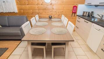 A dining table with six chairs, a kitchen area with a sink and stove, and a wooden wall with a clock.